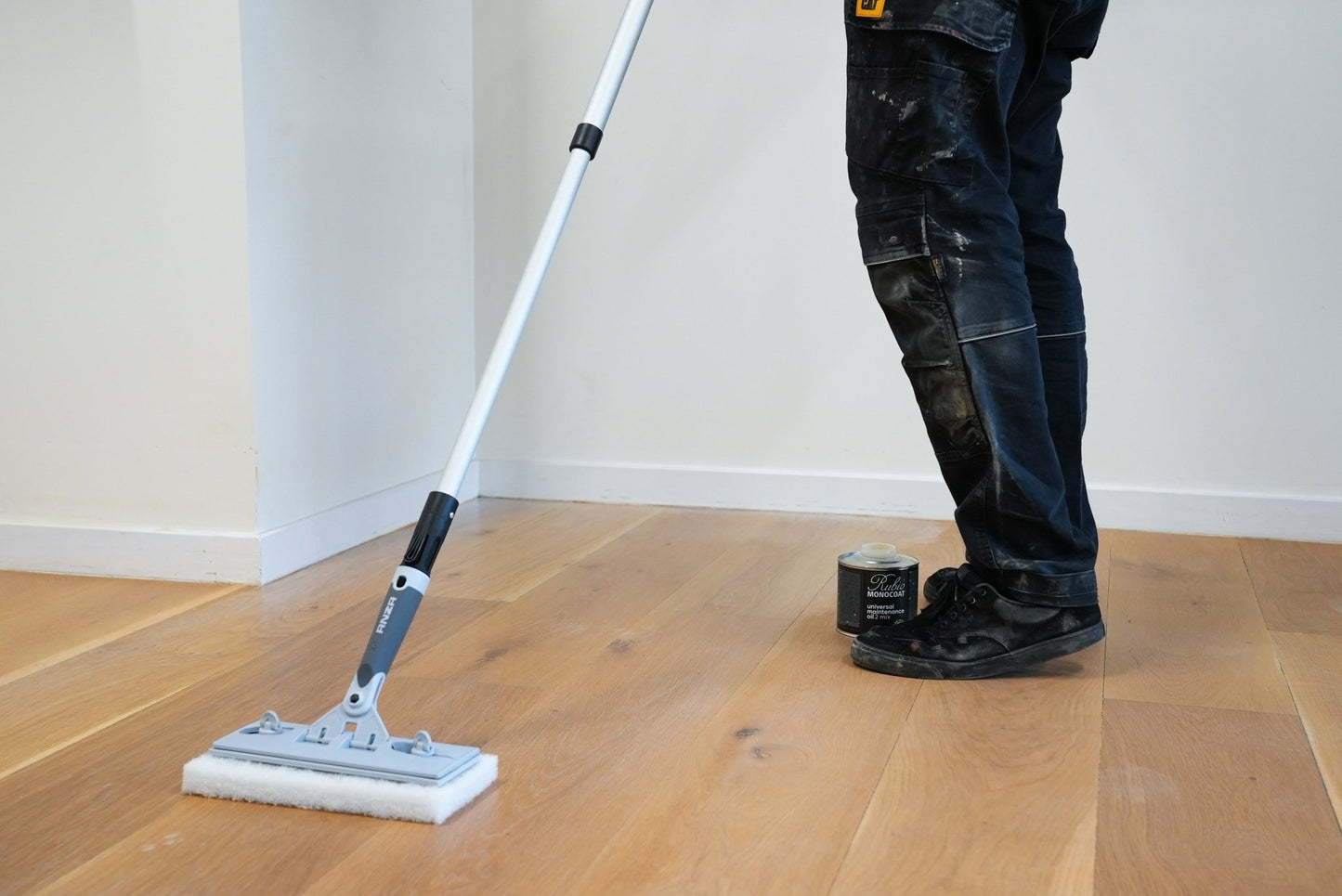 Person cleaning a wooden floor with a pad.