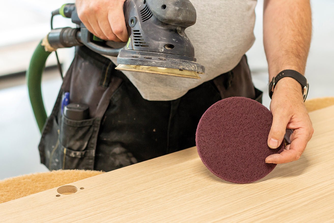 Person using a sander on a wooden surface with a sanding disc in hand.